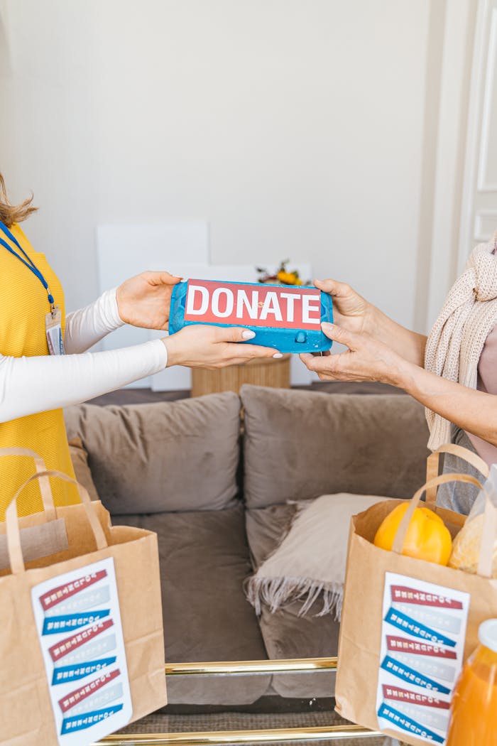 Two people exchanging a donation package indoors with bags of food supplies visible.